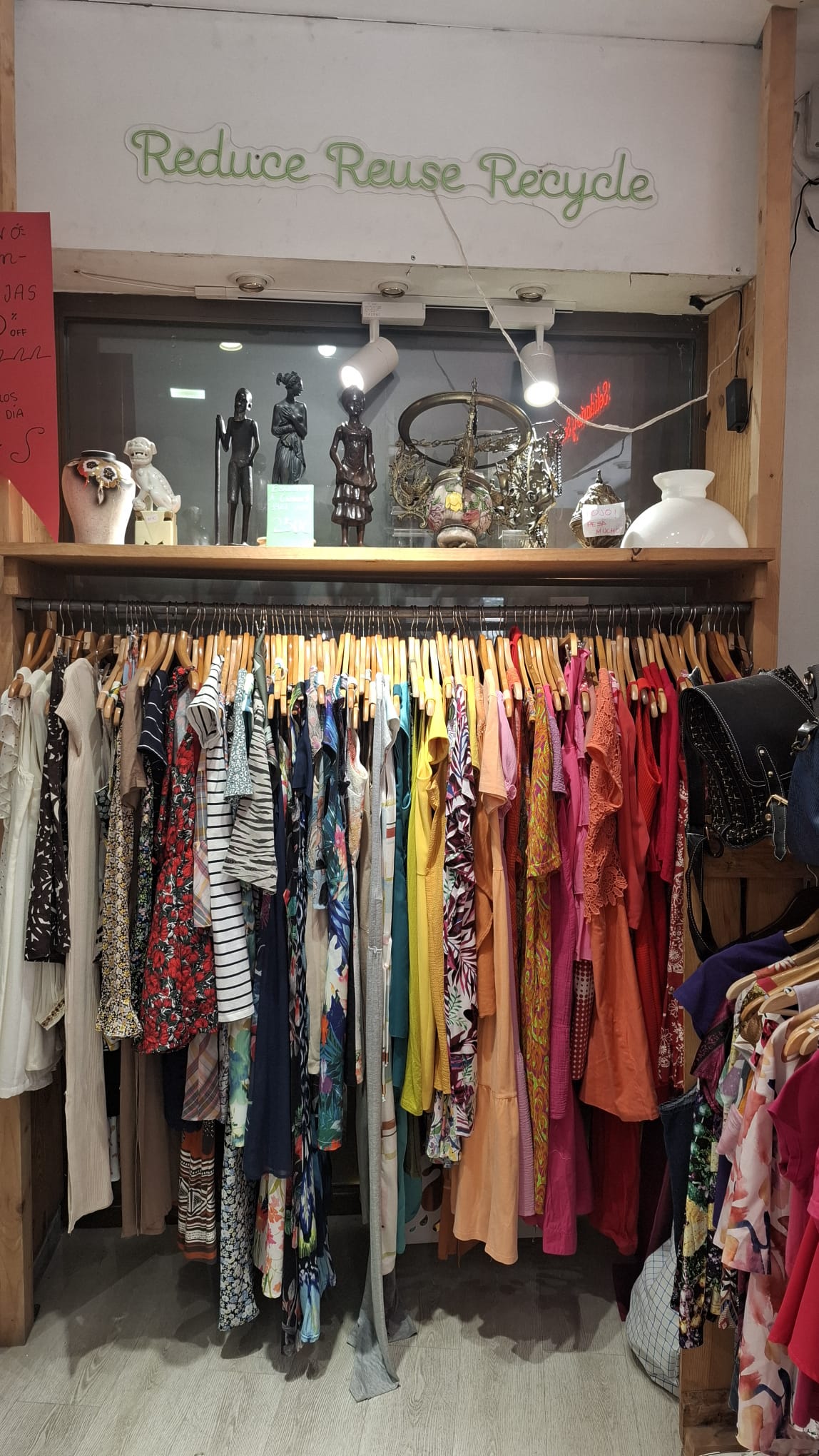 Schaufenster des Joan Charity Shop in Málaga mit Dekoartikeln und der Leuchtschrift „Reduce Reuse Recycle“.